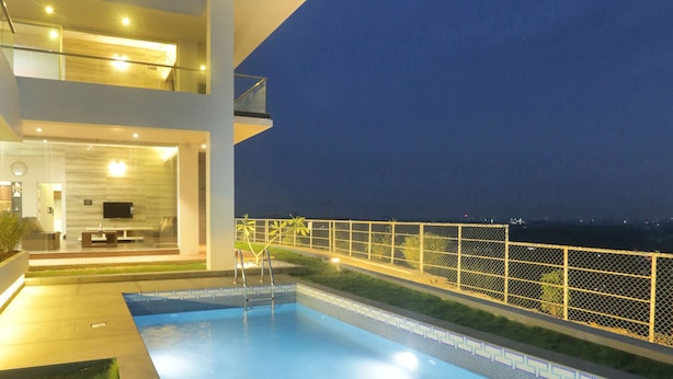 Une maison moderne dotée d’une piscine, d’un balcon et offrant une vue sur la ville la nuit.