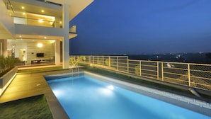 Une maison moderne dotée d’une piscine, d’un balcon et offrant une vue sur la ville la nuit.