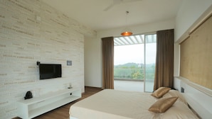 Une chambre moderne avec un grand lit, un téléviseur fixé au mur et une vue sur l’extérieur grâce à une grande fenêtre.