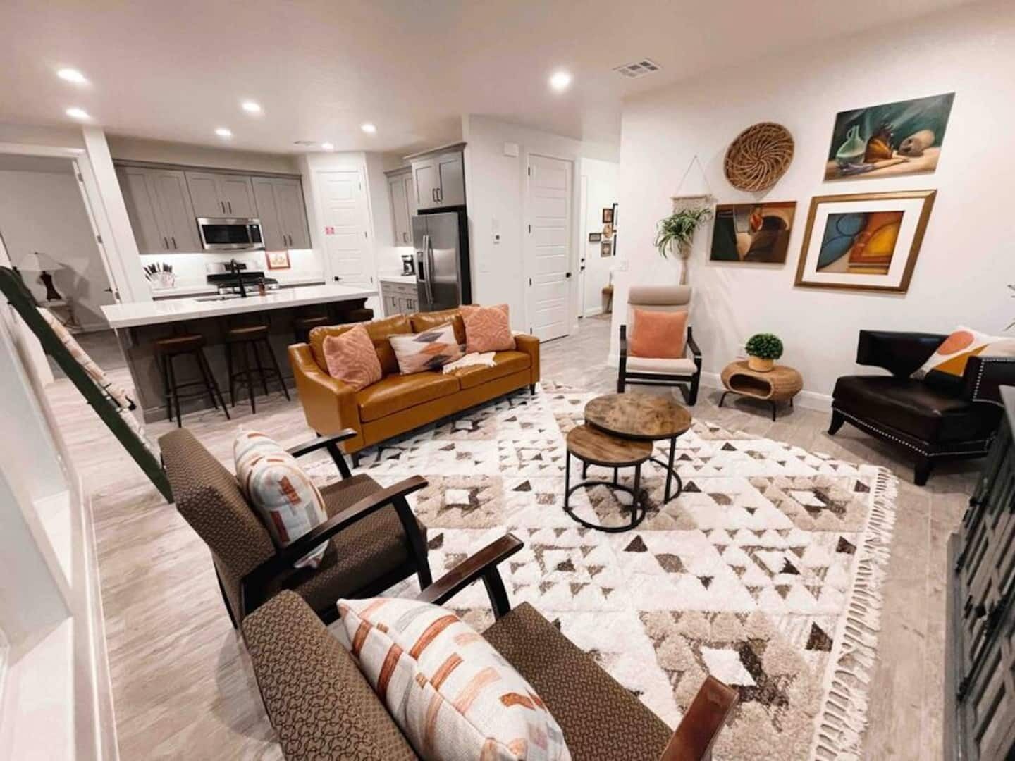 A modern living room with a sofa, armchair, and coffee table, a kitchen in the background, and artwork on the walls.