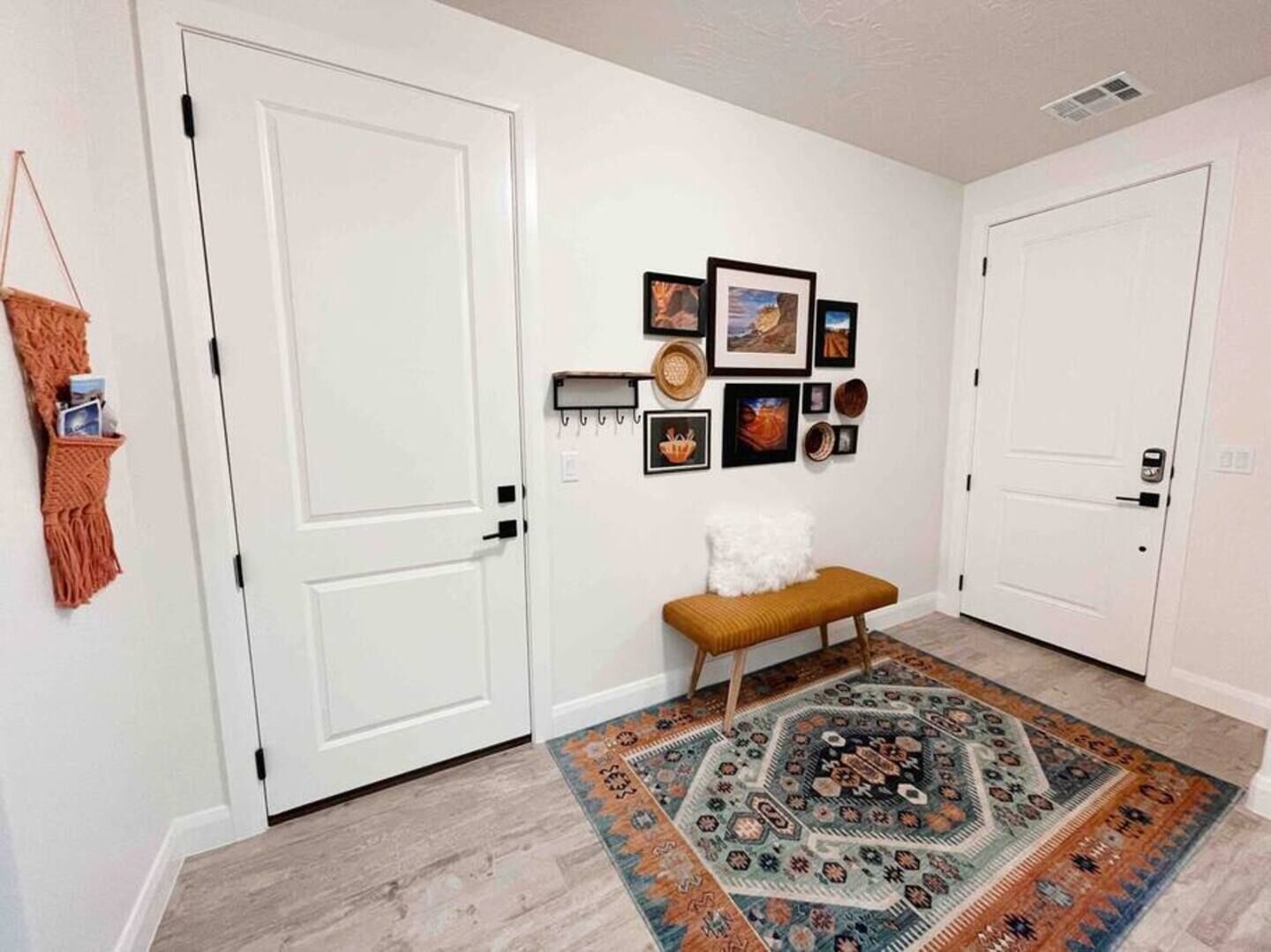 A hallway with two white doors, a bench, a rug, and wall-mounted pictures.