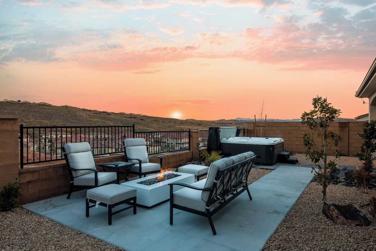 Une terrasse sur le toit, aménagée avec du mobilier d’extérieur, un foyer et un jacuzzi, offrant une vue sur un paysage vallonné au coucher du soleil.
