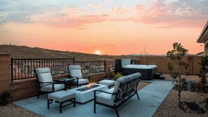 Eine Dachterrasse mit Gartenmöbeln, einer Feuerstelle und einem Whirlpool, mit Blick auf eine hügelige Landschaft bei Sonnenuntergang.