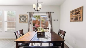 A dining area with a wooden table, chairs, and a chandelier. There is a window with blinds, a decorative wall piece, and a sign on the wall. - Southern Utah charm. Close to St George and National Parks (Washington)