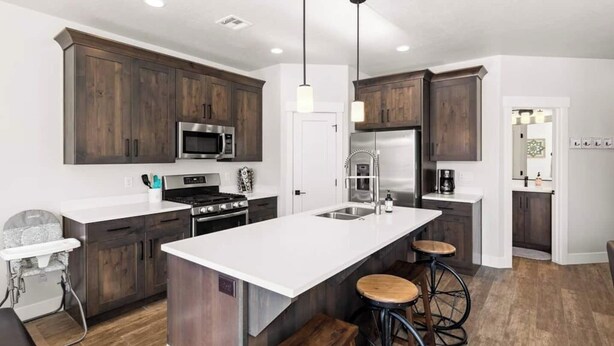 A modern kitchen with dark wood cabinets, stainless steel appliances, a white countertop, and a central island with stools. - Southern Utah charm. Close to St George and National Parks (Washington)