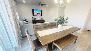 Un comedor con mesa de madera, bancos y un televisor al fondo.