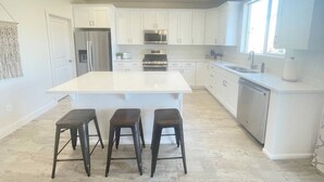 Una cocina moderna con armarios blancos, una isla central y tres taburetes.