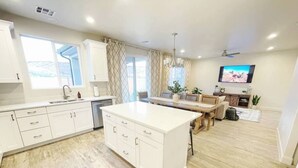 Una cocina moderna con armarios blancos, una isla central y un comedor con mobiliario de madera.