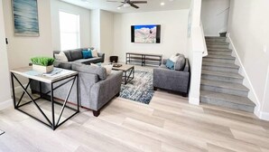A spacious living room with a grey sectional sofa, a coffee table, and a TV mounted on the wall.