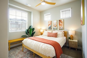 A bedroom with a bed, bedside lamps, a bench, and a large plant.