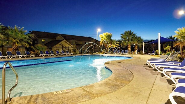 A swimming pool with lounge chairs and palm trees, surrounded by buildings.