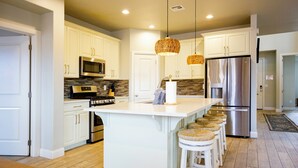 A modern kitchen with white cabinetry, stainless steel appliances, a large island with bar stools, and pendant lighting.