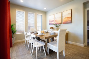 A dining area with a wooden table set for four, white chairs, and a vase with flowers.