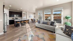 A spacious living area with a grey sofa, a kitchen with dark cabinets, and a large window offering a view of the outdoors. - Southern Utah charm. Close to St George and National Parks (Washington)