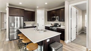 A modern kitchen with dark wood cabinets, stainless steel appliances, a large island with stools, and a view into the adjacent living area. - Southern Utah charm. Close to St George and National Parks (Washington)