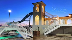 Ein Wasserpark mit Rutsche, Schwimmbecken und einem Gebäude mit Turm und Treppe.