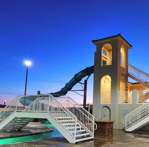 A water park with a slide, a pool, and a building with a tower and stairs.