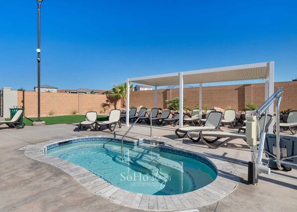 A swimming pool with lounge chairs and a covered area, surrounded by a brick wall and a clear blue sky.