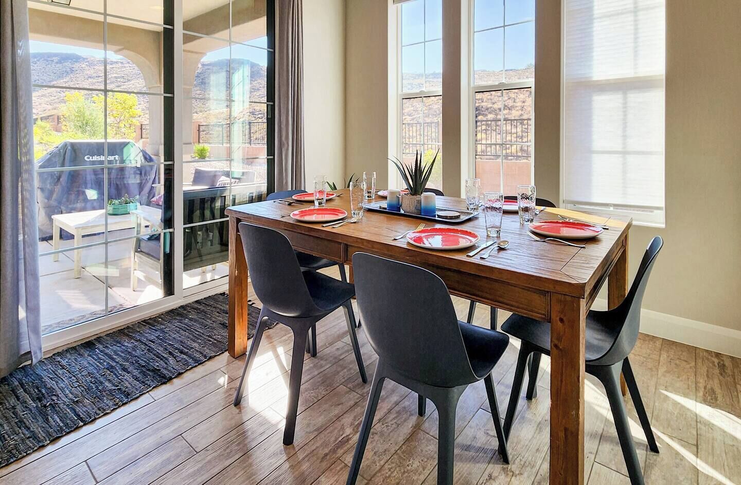 A dining area with a wooden table set for four, black chairs, and a view of a mountainous landscape through large windows.