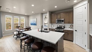 Una cocina moderna con una isla central, taburetes de bar y un comedor con vistas al exterior.