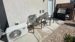 An outdoor patio with a grill, a table and chairs, and an air conditioning unit.