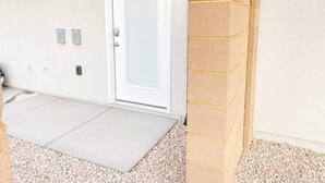 A white door with a window, a wall-mounted light fixture, and a small outdoor area with a concrete floor and gravel.