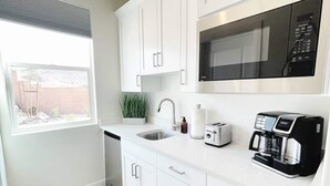 A modern kitchen with white cabinets, a stainless steel sink, a microwave, a toaster, and a coffee maker.