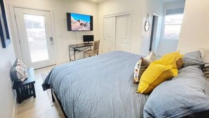 A bedroom with a bed, a desk, a chair, a television, and a ceiling fan.