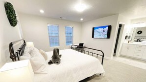 A bedroom with a bed, bedside table, lamp, and a TV on the wall.