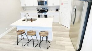 A modern kitchen with white cabinets, a central island with stools, stainless steel appliances, and a wooden floor.