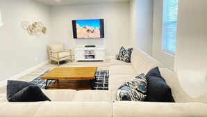 A modern living room with a beige sofa, a wooden coffee table, a white entertainment unit, and a flat-screen TV mounted on the wall.
