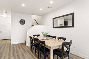 A dining area with a wooden table and chairs, a potted plant, a clock, and a mirror on the wall.
