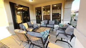 Patio esterno con mobili in vimini e tavolo in legno, ampie finestre e vista sui dintorni.