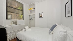 A bedroom with a bed, a dresser, a window with blinds, a radiator, and a shelf with towels. - Private and Cozy  3 Bedroom in the heart of Manhattan.  (New York)