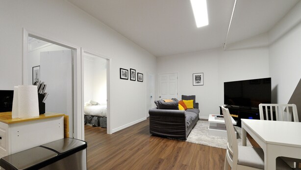 A modern living room with a sofa, a TV, a dining table, and a trash bin. - Private and Cozy  3 Bedroom in the heart of Manhattan.  (New York)