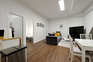 Una sala de estar moderna con un sofá, un televisor, una mesa de comedor y un cubo de basura.