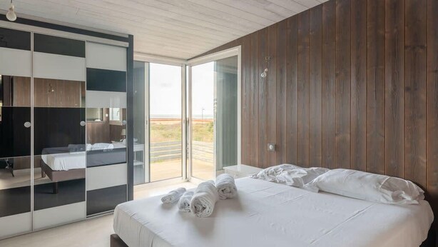 A modern bedroom with a large bed, a wardrobe with sliding doors, and a view of the outdoors through a glass door. - La Tara - Vue mer - Parking - Terrasse (La Plaine-sur-Mer)