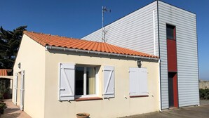 A two-story building with a red-tiled roof, white siding, and a small attached garage with a red door. - La Tara - Vue mer - Parking - Terrasse (La Plaine-sur-Mer)