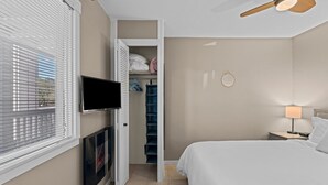Une chambre à coucher comprenant un lit, un téléviseur fixé au mur, un ventilateur de plafond et une armoire avec des étagères.