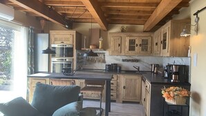 A rustic kitchen with wooden cabinets, a marble countertop, and a dining area with a bench. - Gemütliche Ferienwohnung, Ideal für 2 Personen, Große Terrasse und Swimming-pool (Arles)