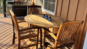 Une terrasse en bois avec une table ronde et des chaises, un barbecue et une fenêtre donnant sur un paysage.