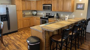 Une cuisine moderne avec des meubles en bois, un réfrigérateur en acier inoxydable, un four à micro-ondes et un grand îlot central doté de tabourets de bar.
