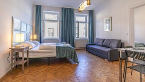 A bedroom with a bed, bedside table, lamp, sofa, and a dining area with chairs.