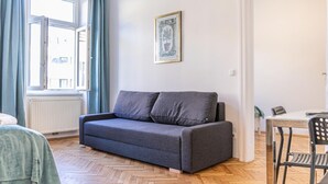 A room with a grey sofa, a dining table with chairs, a radiator, and a window with curtains.