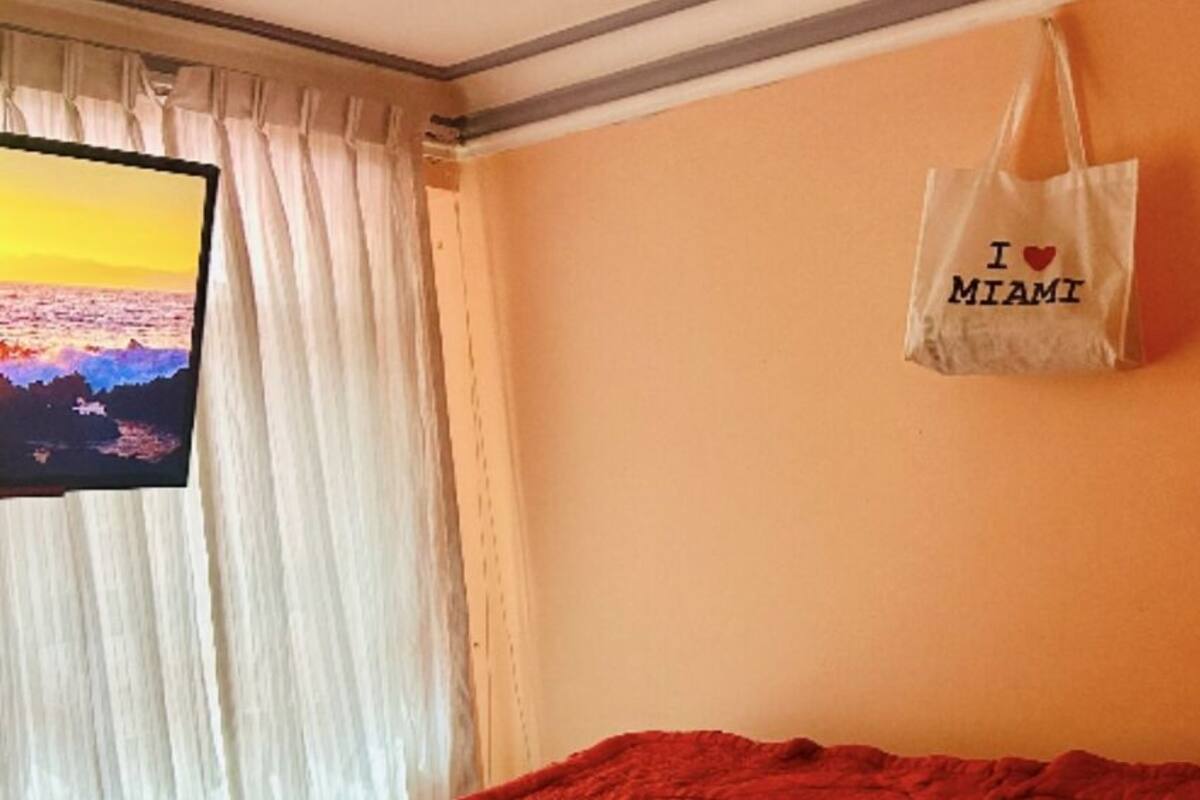 Ein Zimmer mit einem Bett, einem Fernseher links und einer Wand mit einer 'I ♥ MIAMI' Tasche.