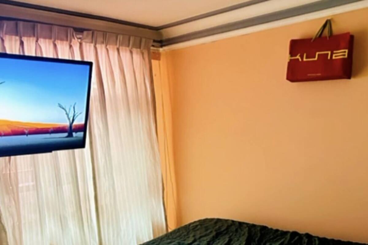 Ein Zimmer mit einem Bett, einem Fernseher links und einer roten Tasche an der Wand.