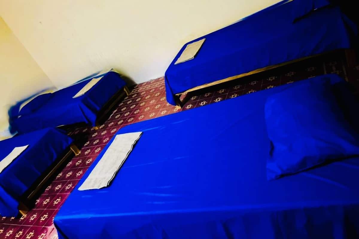Ein Zimmer mit vier Einzelbetten, jedes mit blauer Bettdecke und passenden Kissen.