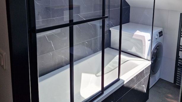 A modern bathroom with a built-in washer and dryer, a skylight, and a black tiled wall. - Appartement Sous Combe Climatisé 2 éme Étage (Publier)