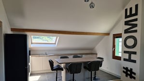 A modern kitchen with a skylight, a dining area with bar stools, and a large wooden table. - Appartement Sous Combe Climatisé 2 éme Étage (Publier)