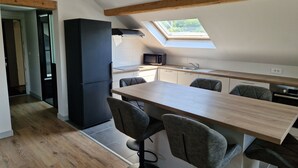 A modern kitchen with a wooden ceiling, a skylight, and a dining area with a table and chairs. - Appartement Sous Combe Climatisé 2 éme Étage (Publier)